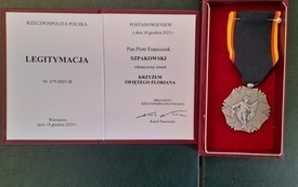 Na zdjęciu, na szarym tle legitymacja i odznaczenie Krzyż Świętego Floriana.