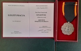 Na zdjęciu, na szarym tle legitymacja i odznaczenie Krzyż Świętego Floriana.