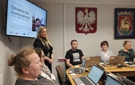Na zdjęciu uczestnicy szkolenia. Przed każdym laptop. Na ścianie, na ekranach wyświetlana prezentacja.