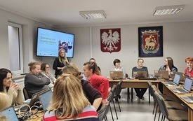 Na zdjęciu uczestnicy szkolenia. Przed każdym laptop. Na ścianie, na ekranach wyświetlana prezentacja.