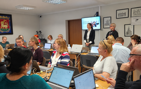 Grupa uczestnik&oacute;w szkolenia w sali. Przed każdym laptop. W tle, na ścianie ekran z wyświetloną prezentacją.