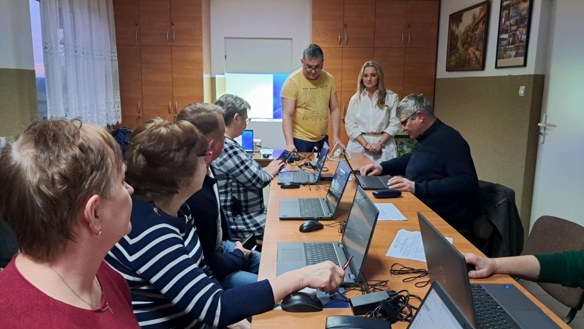 Osoby znajdują sie w&nbsp;pomieszczeniu. Kobiety i&nbsp;mężczyźni siedzą przy stolikach, na&nbsp;kt&oacute;rych są laptopy.