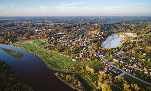 Zdjęcie przedstawia rzekę, tereny zielone oraz panoramę niewielkiej miejscowości.