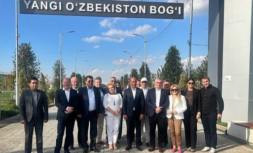 Na zdjęciu przedstawiciele firm i samorządów stojący na chodniku. U góry znak z napisem YANGI O'ZBEKISTON BOG'I.